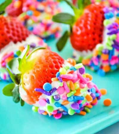 White chocolate dipped strawberries covered in rainbow sprinkles on a turquoise plate.