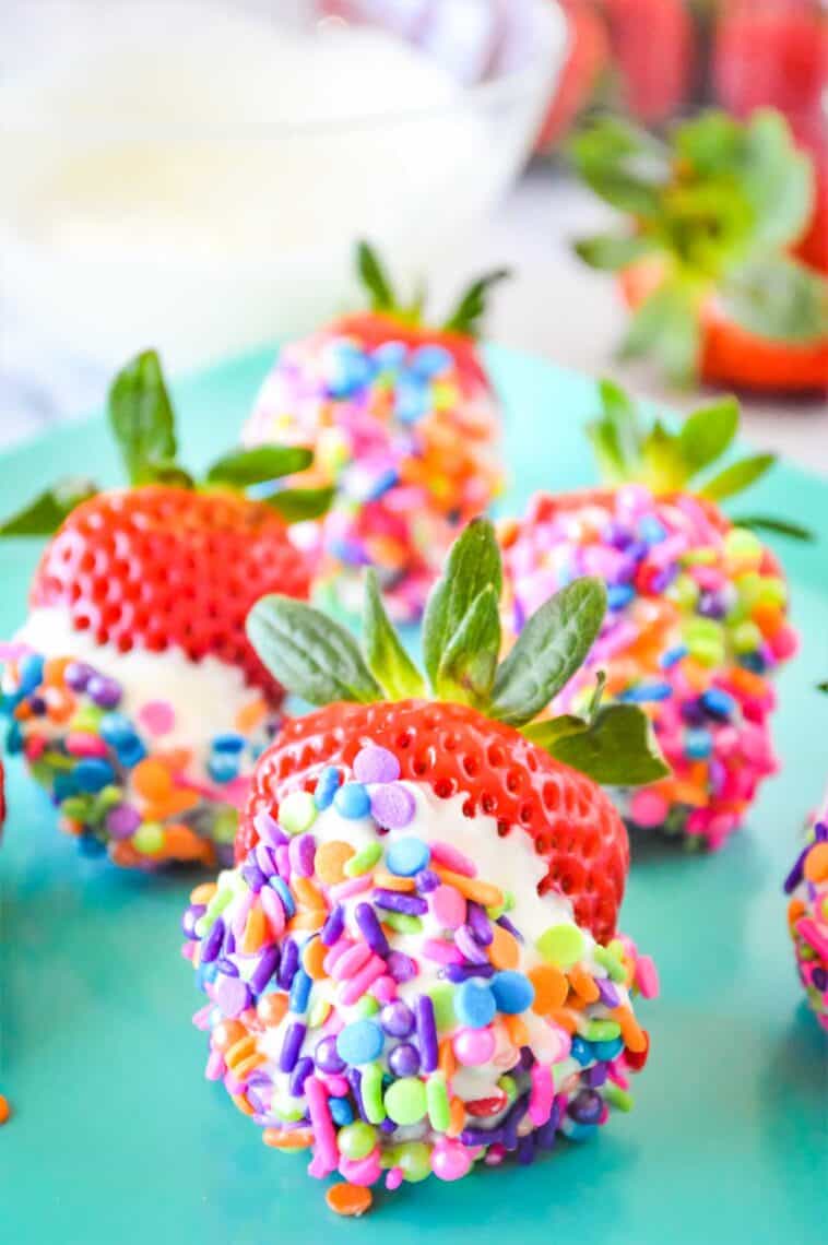 A turquoise plate with white chocolate strawberries dipped in sprinkles.