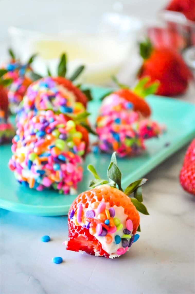 One white chocolate covered strawberry with a bite taken out and the rest on a platter.