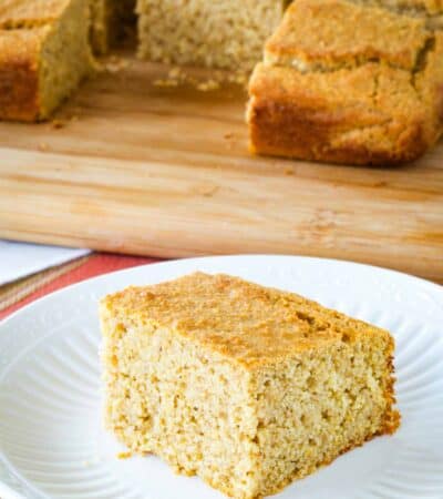 A piece of apple butter cornbread on a plate with the rest of the cornbread on a cutting board in the background.