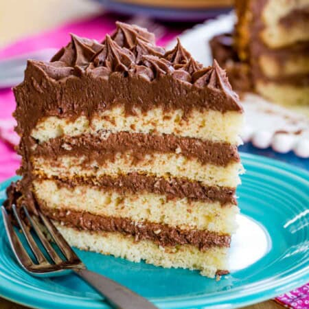 A slice of gluten free layer cake with chocolate buttercream on a plate with a fork.