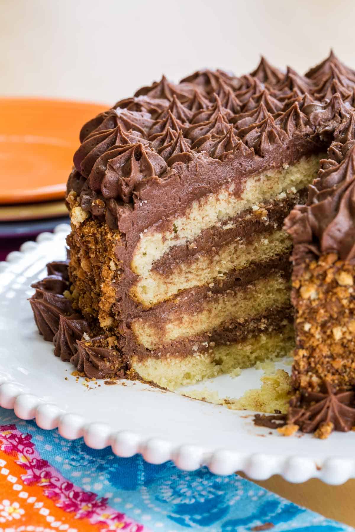 A yellow layer cake with chocolate frosting on a platter with a slice removed.