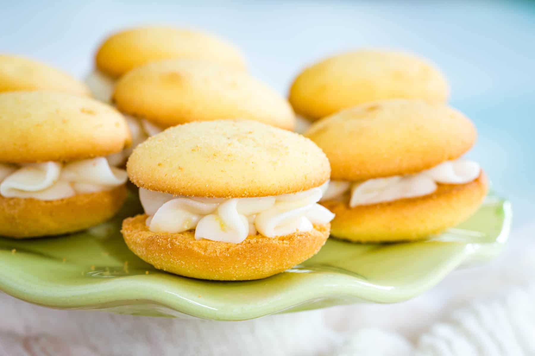 Several small sandwich cookies on a pale green platter with a scalloped edge.