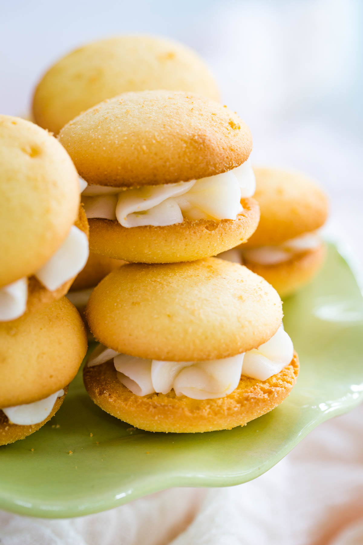 Gluten Free Lemon Sandwich Cookies stacked on a small light green cake plate.