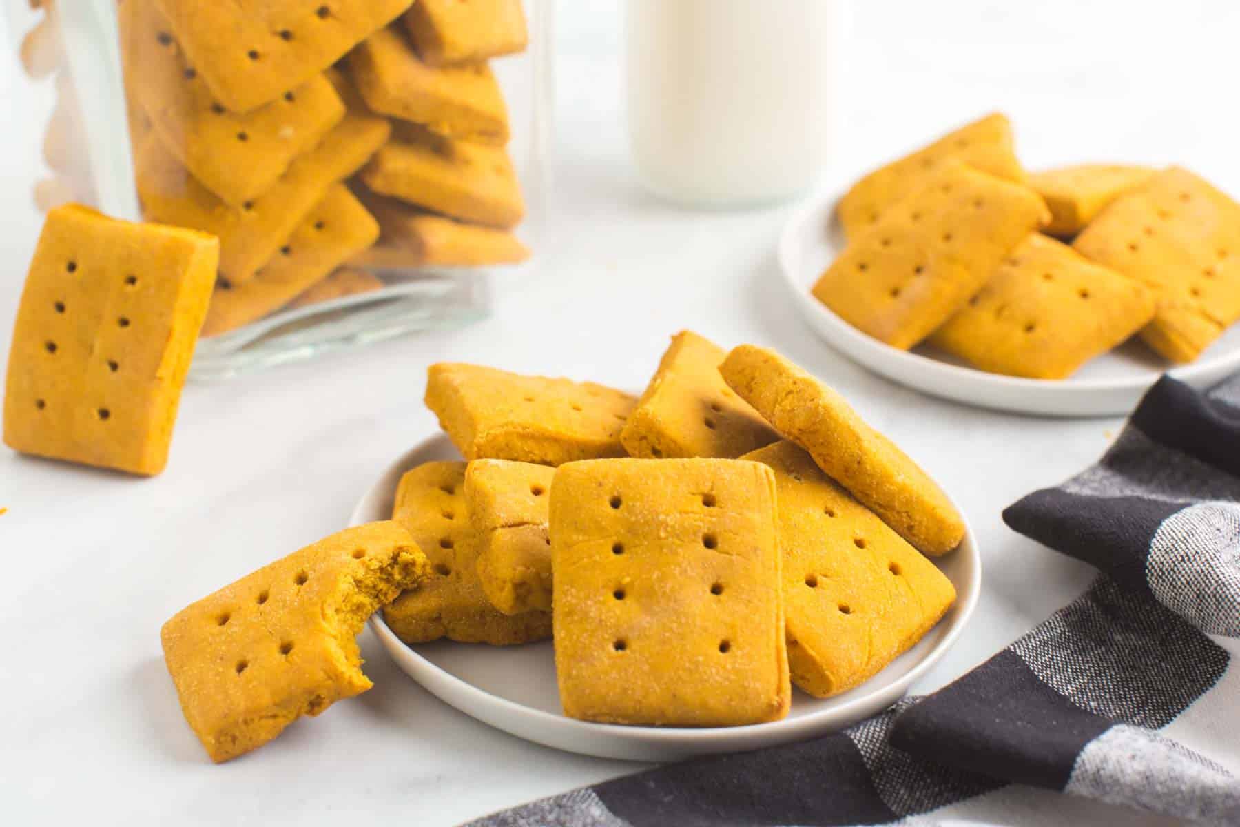 gluten free pumpkin graham crackers on plates and in a jar with a bite taken out of one cookie.