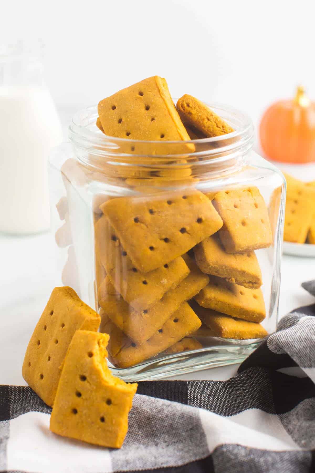 a glass jar fill of gluten free pumpkin graham crackers on a black and white cloth napkin with two cookies leaning against the jar.