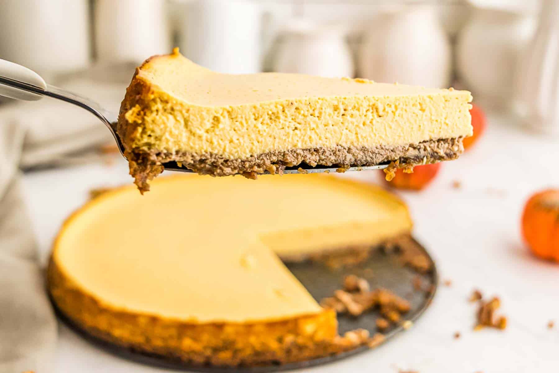 A pie server holding up a slice of gluten free pumpkin cheesecake tart over the rest of the tart.