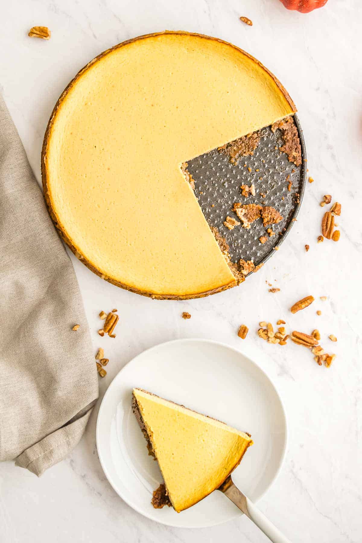 A pie server putting a piece of pumpkin tart on a plate and the rest of the tart on the base of the springform pan surrounded by chopped pecans.