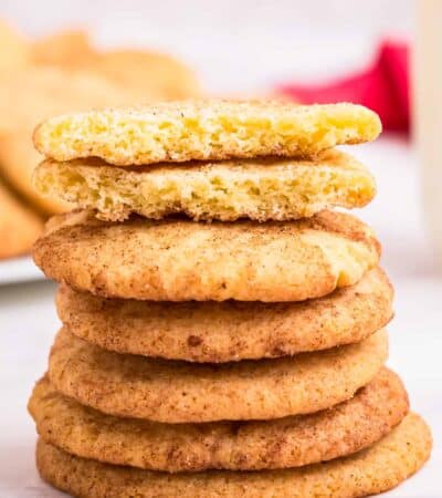 A stack of snickerdoodle cookies with one on top broken in half to show the interior texture.