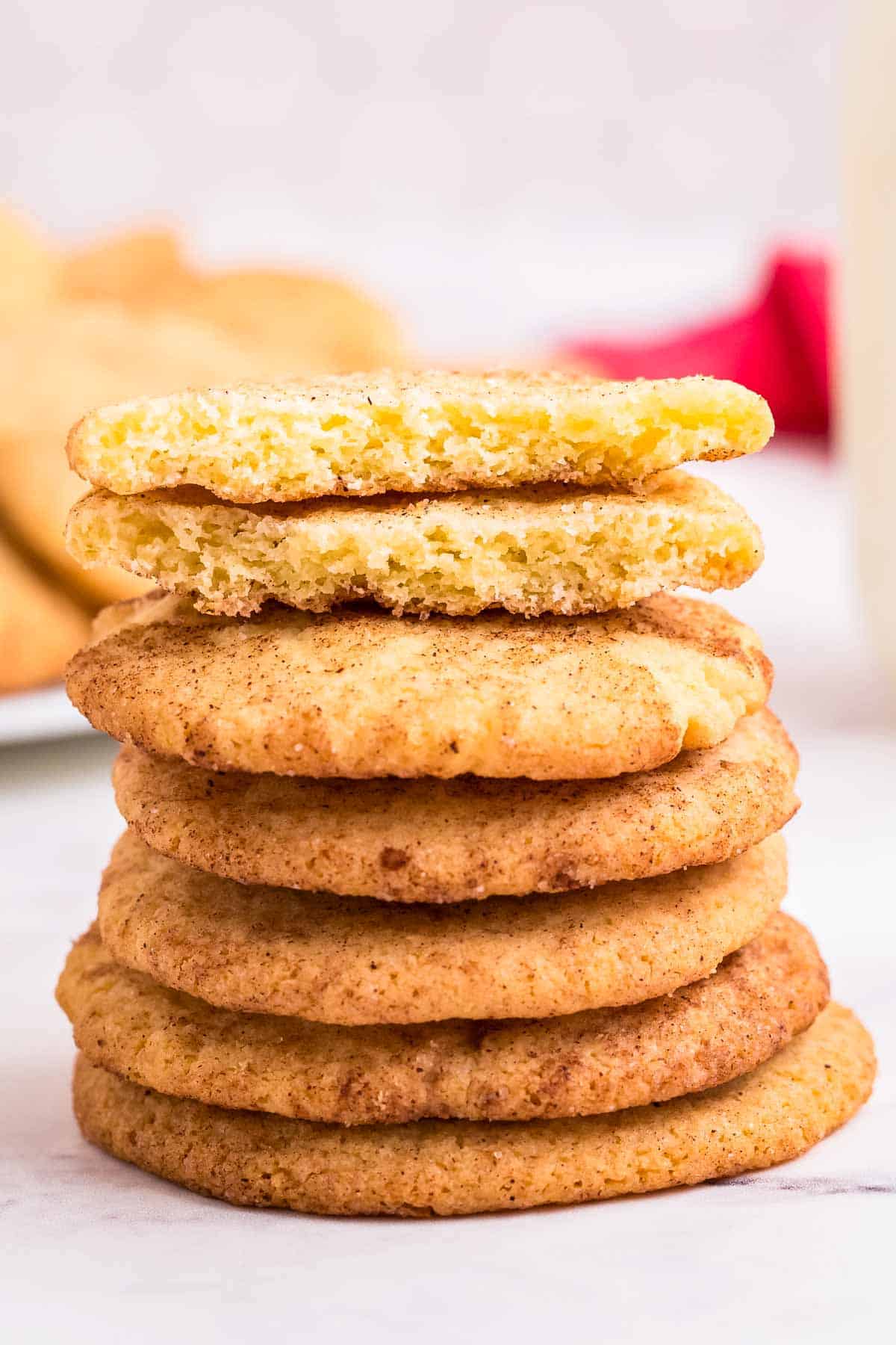 A stack of snickerdoodle cookies with one on top broken in half to show the interior texture.
