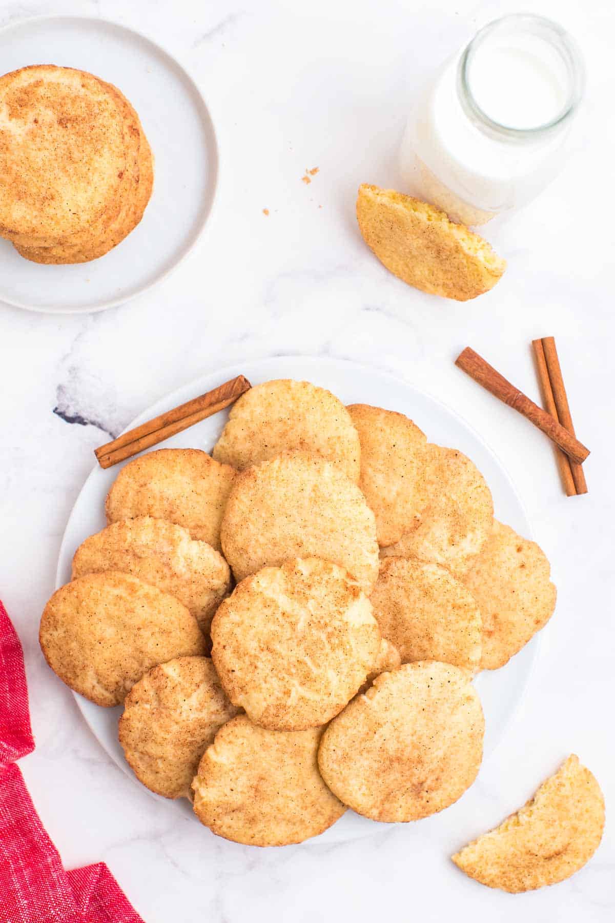 Gluten Free Snickerdoodles spread on a plate with a stack on a smaller plate and a glass of milk.