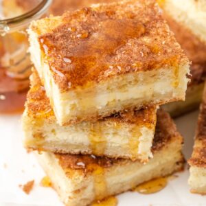 A stack of gluten free sopapilla cheesecake bars dripping with honey.