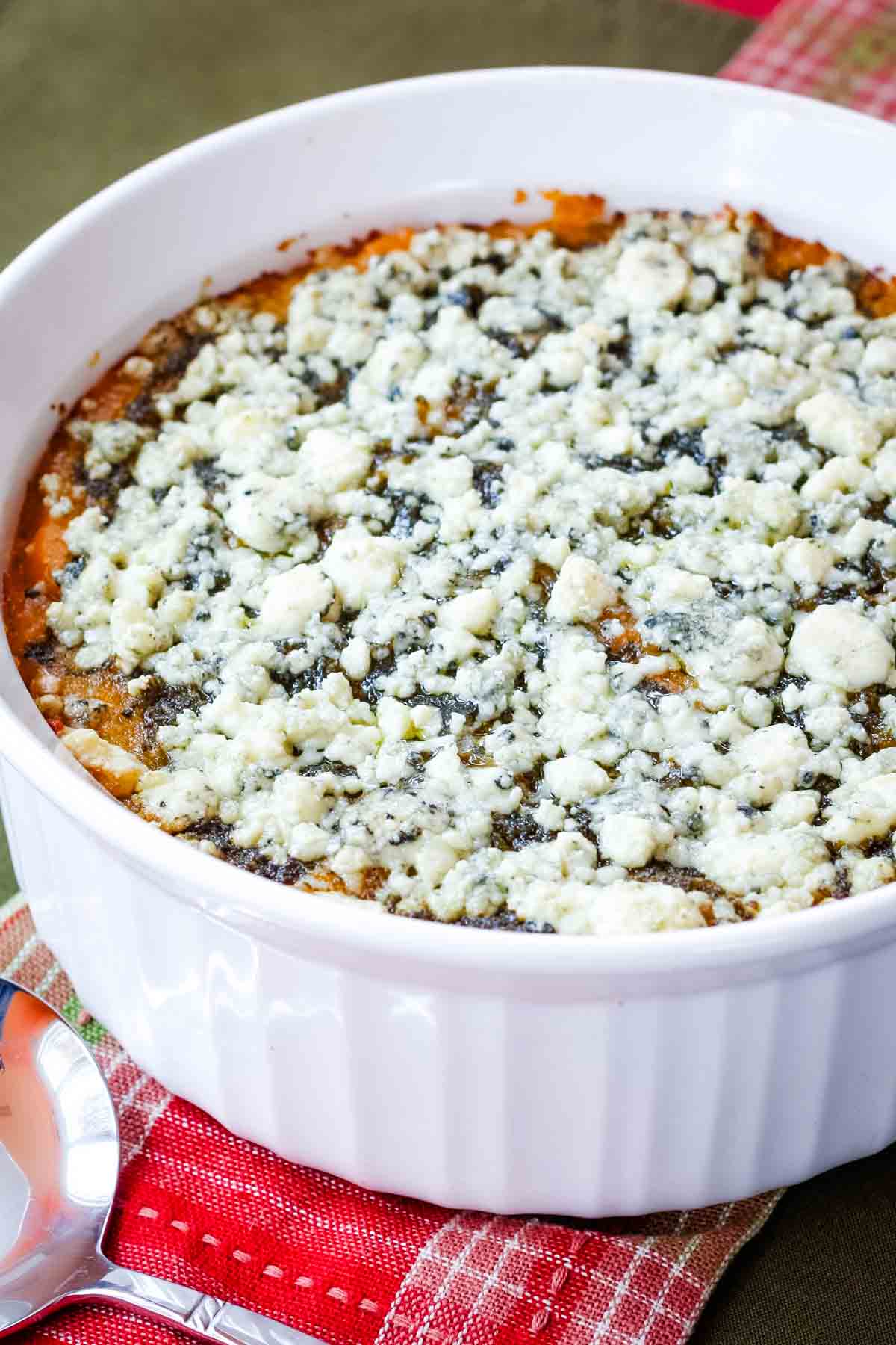 A baked butternut squash casserole topped with crumbled blue cheese in a round white ceramic dish.