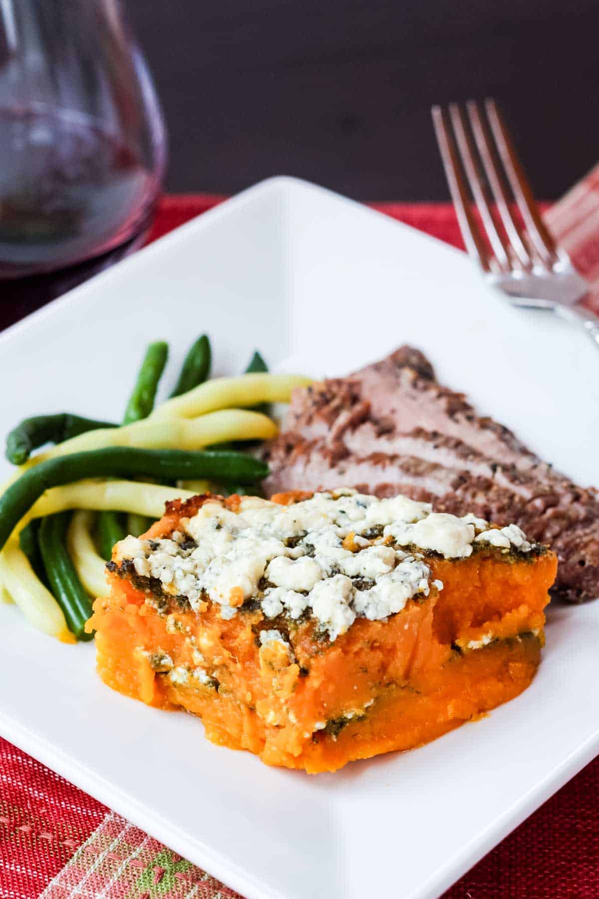 A scoop of Butternut Squash Gratin on a plate with steak and string beans.
