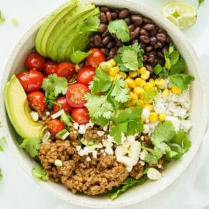 A birds-eye view of a ground beef burrito bowl with lime wedge off to the side.