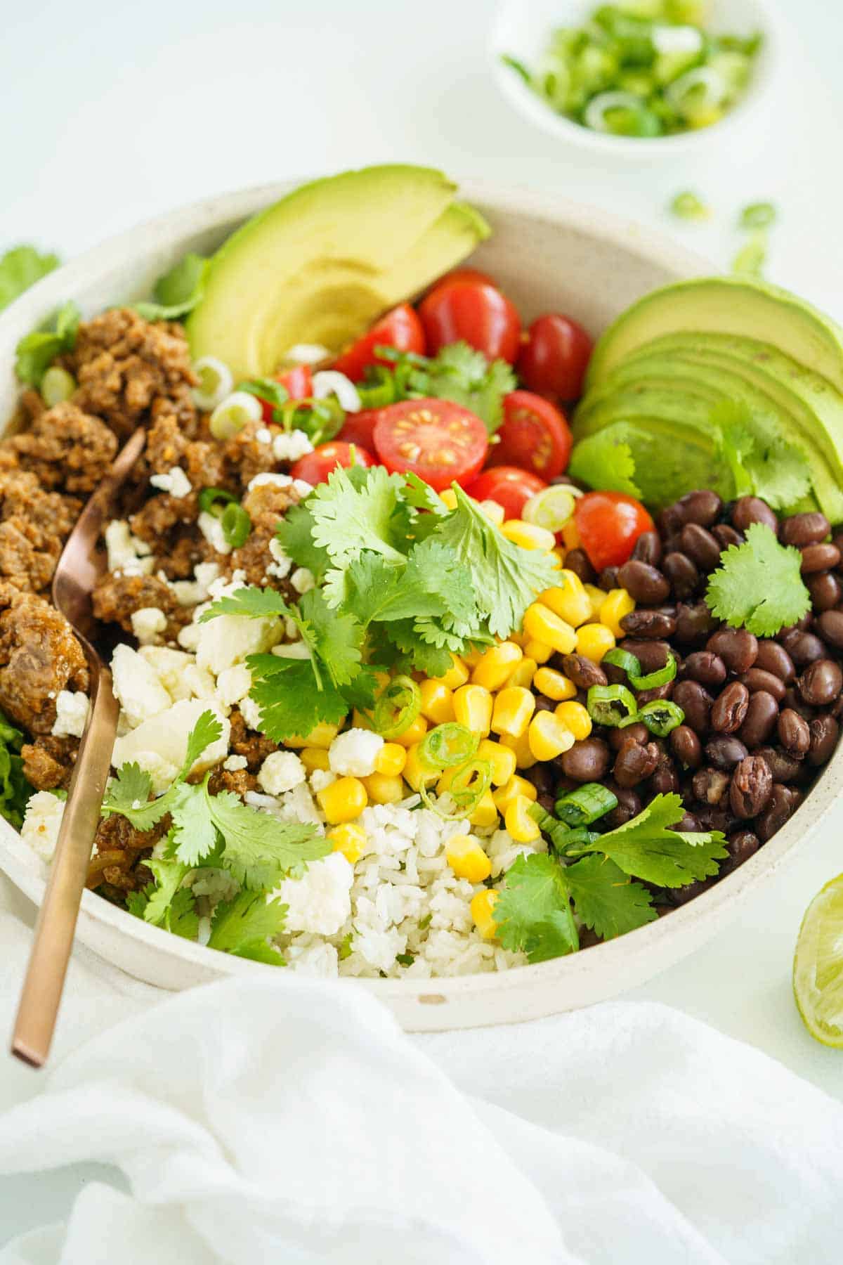 A fok in a ground beef burrito bowl topped with beans, corn, cheese, and cilantro.