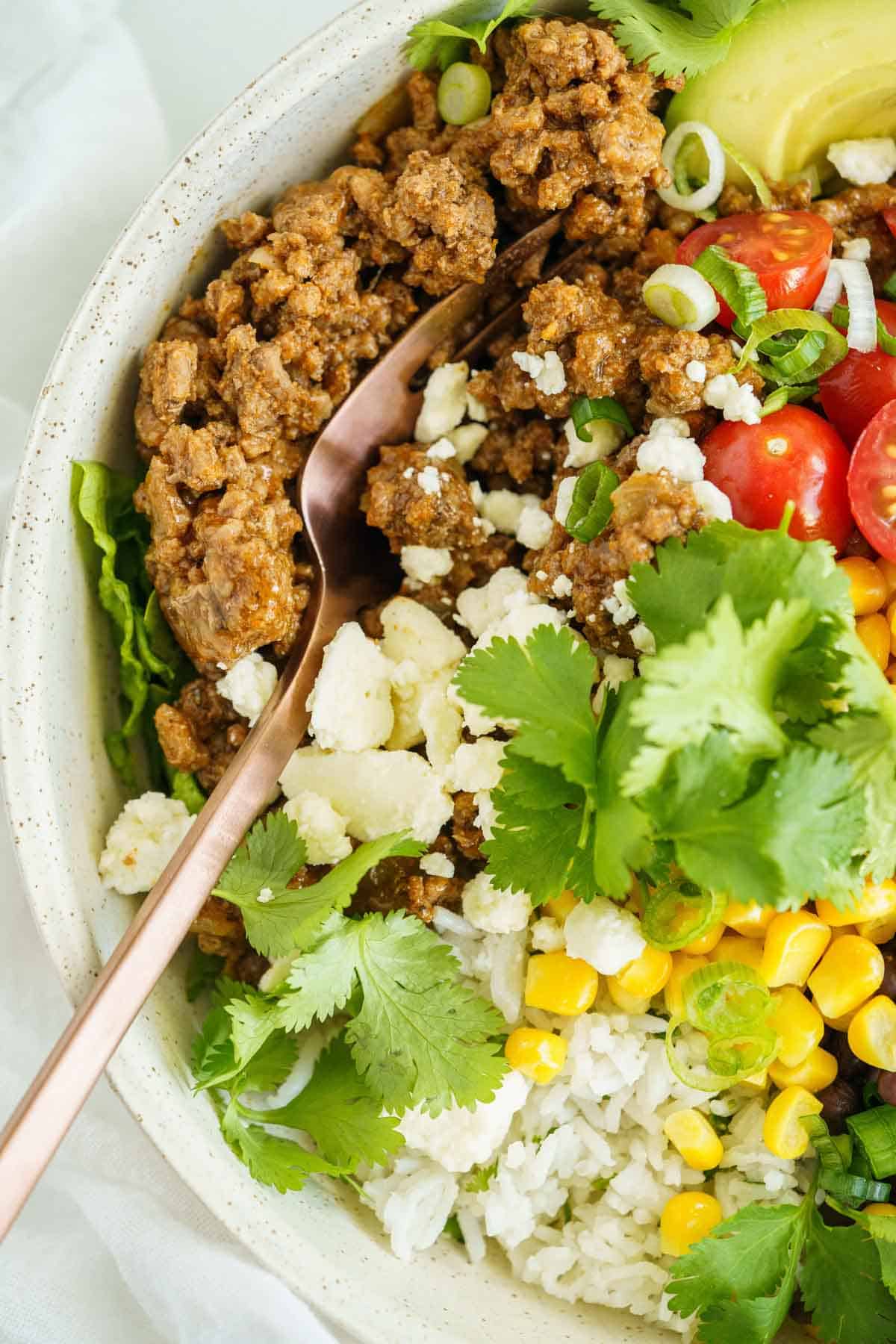 A closeup of a fork stuck in the ground beef taco meat on top of a burrito bowl.