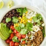 A beef and rice bowl with taco toppings on a white table with a white napkin and squeezed lime wedges with text overlay that says "Ground Beef Burrito Bowls".