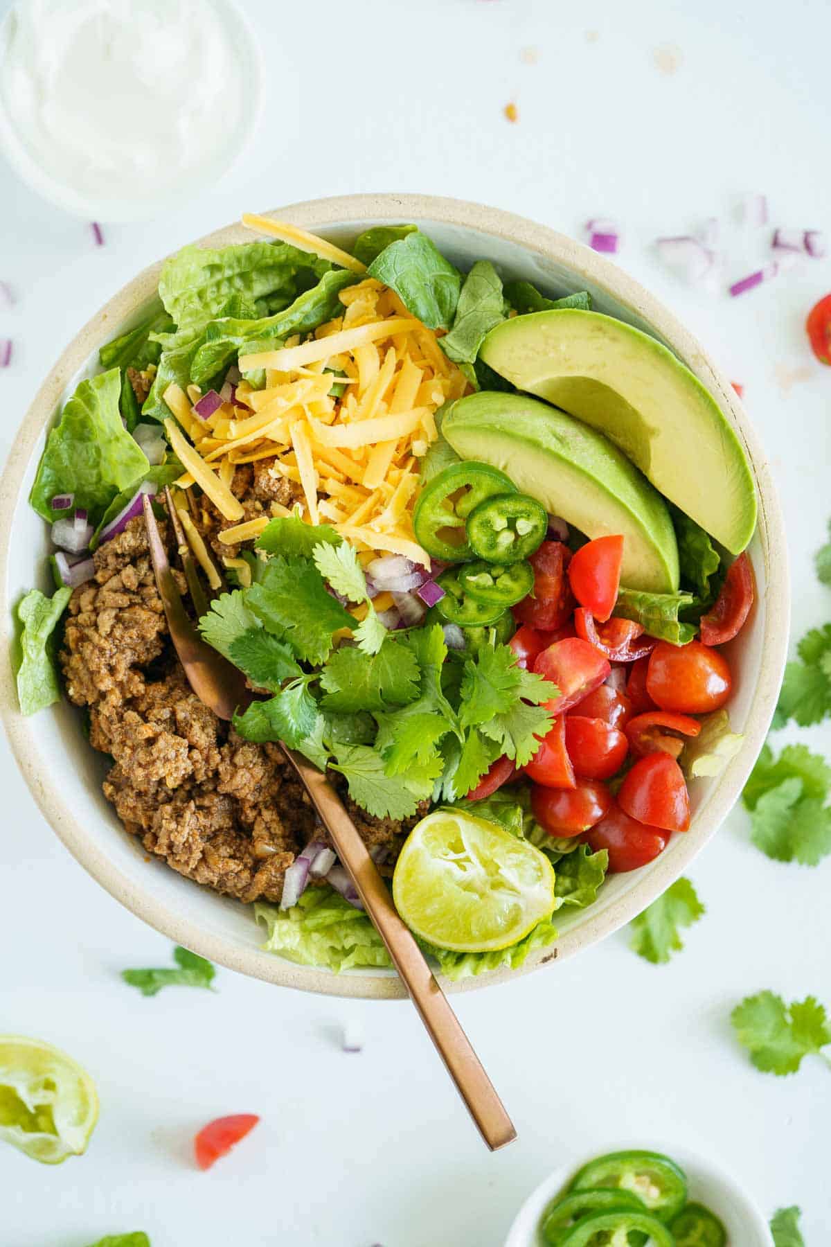 An overhead view of a ground beef taco bowl with a fork on the meat partially under the cilantro.