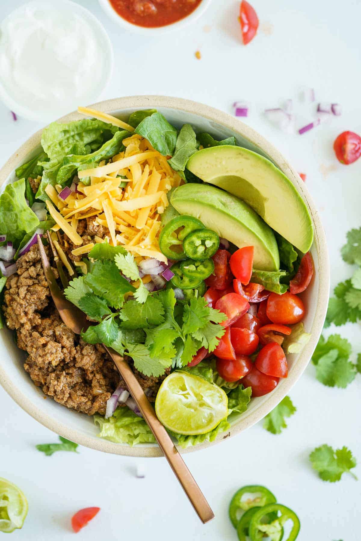A birds-eye view of a ground beef taco salad with a fork in it and some of the toppings scattered on the countertop.