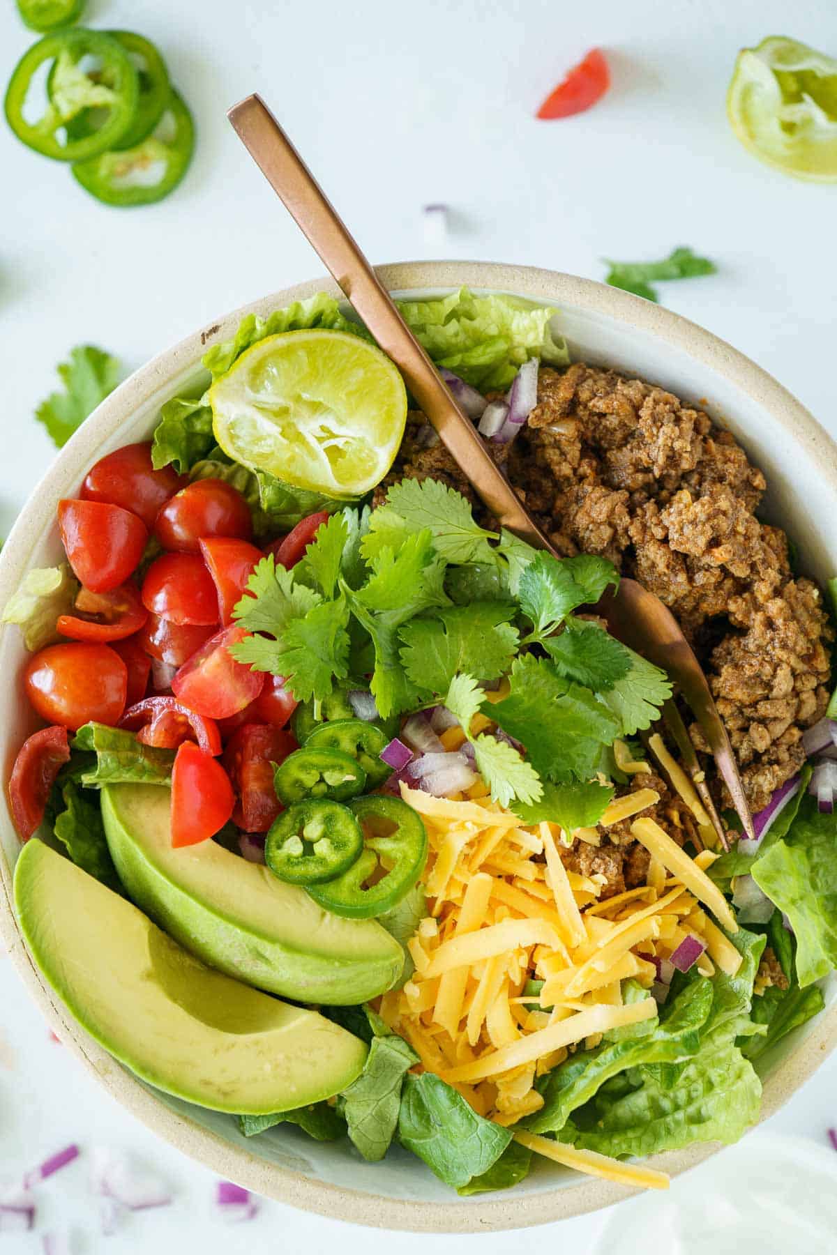 A fork dug into a taco bowl with lettuce, ground beef taco meat and lots of fixings.