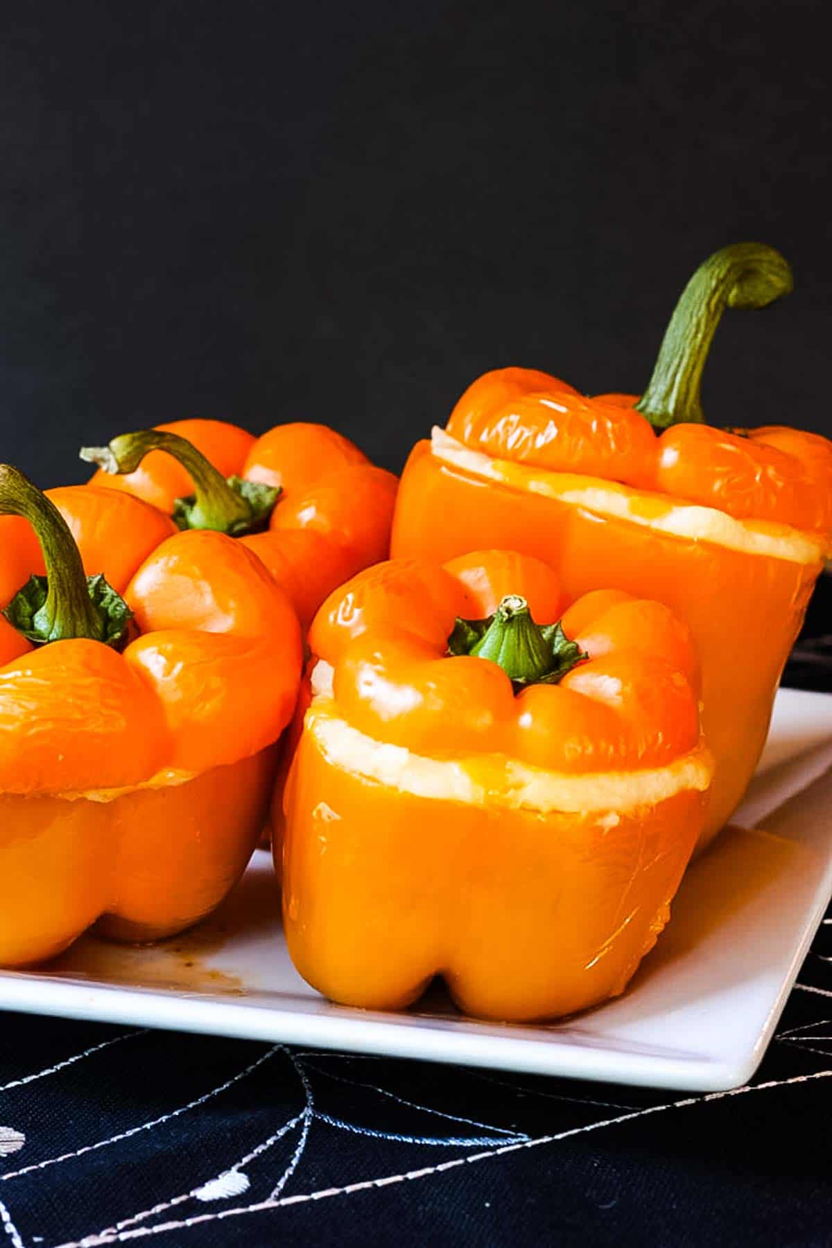 Four orange stuffed peppers on a plate with the mashed potatoes topping peeking out.