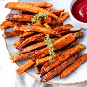 A plate of baked sweet potato fries garnished with fresh herbs.