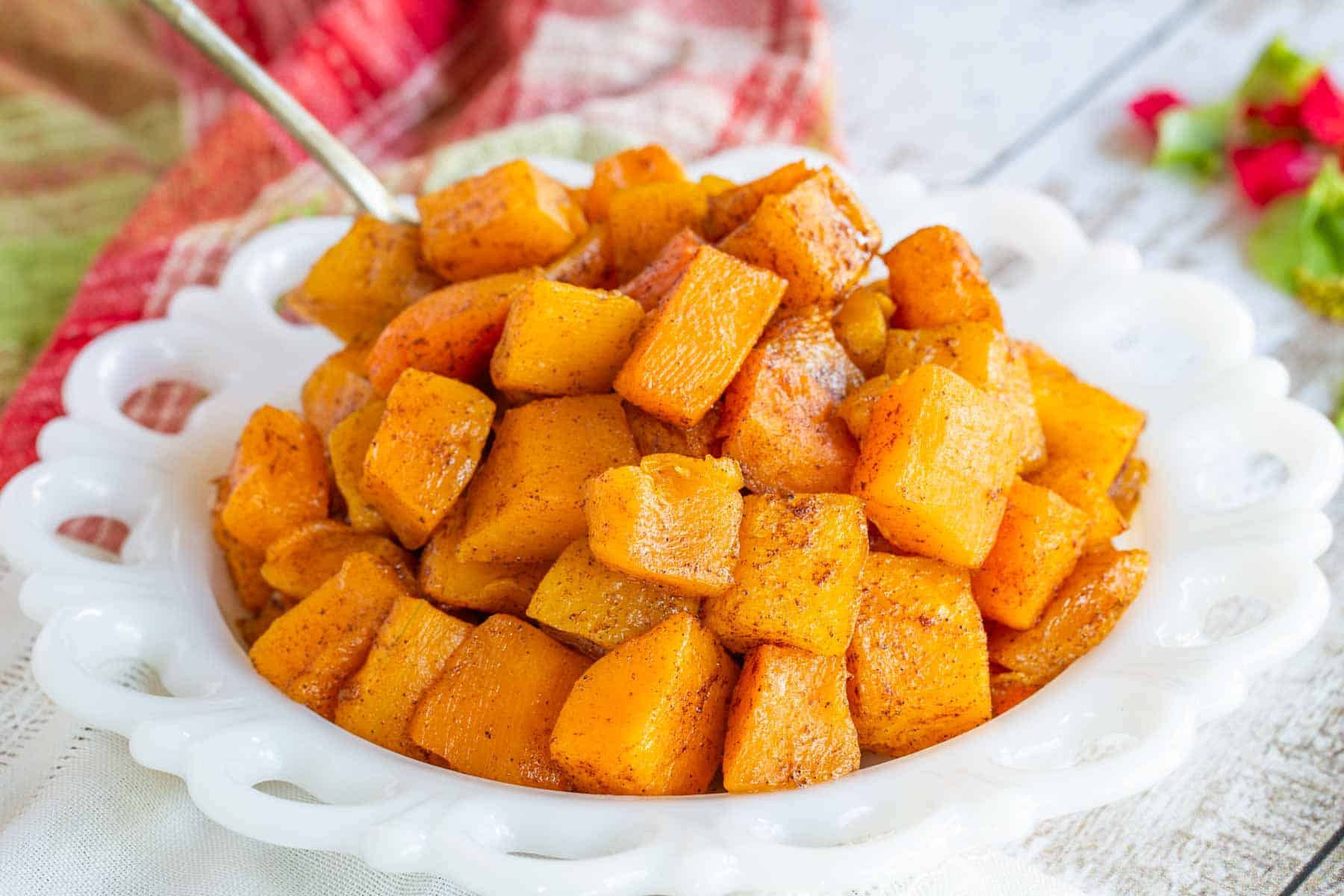 A white plate with a pile of cinnamon roasted butternut squash with a serving spoon in it.