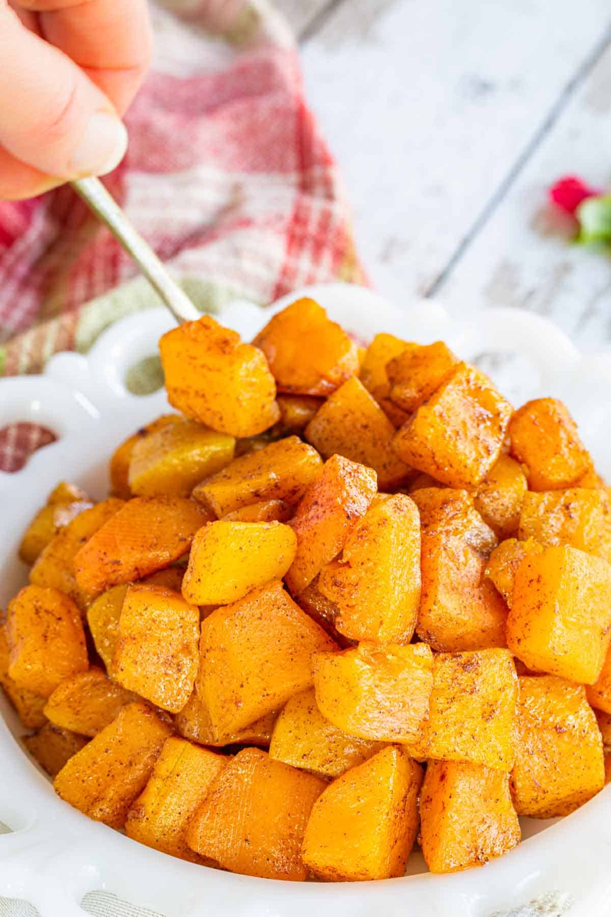 A hand holding a spoon scooping up roasted butternut squash cubes.