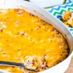 A pan of pork roll and cheese dip with a bowl of bagel chips in the background.