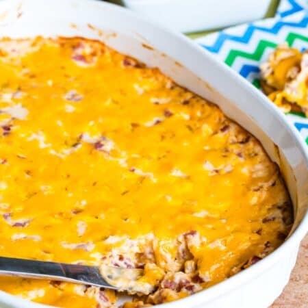 A pan of pork roll and cheese dip with a bowl of bagel chips in the background.