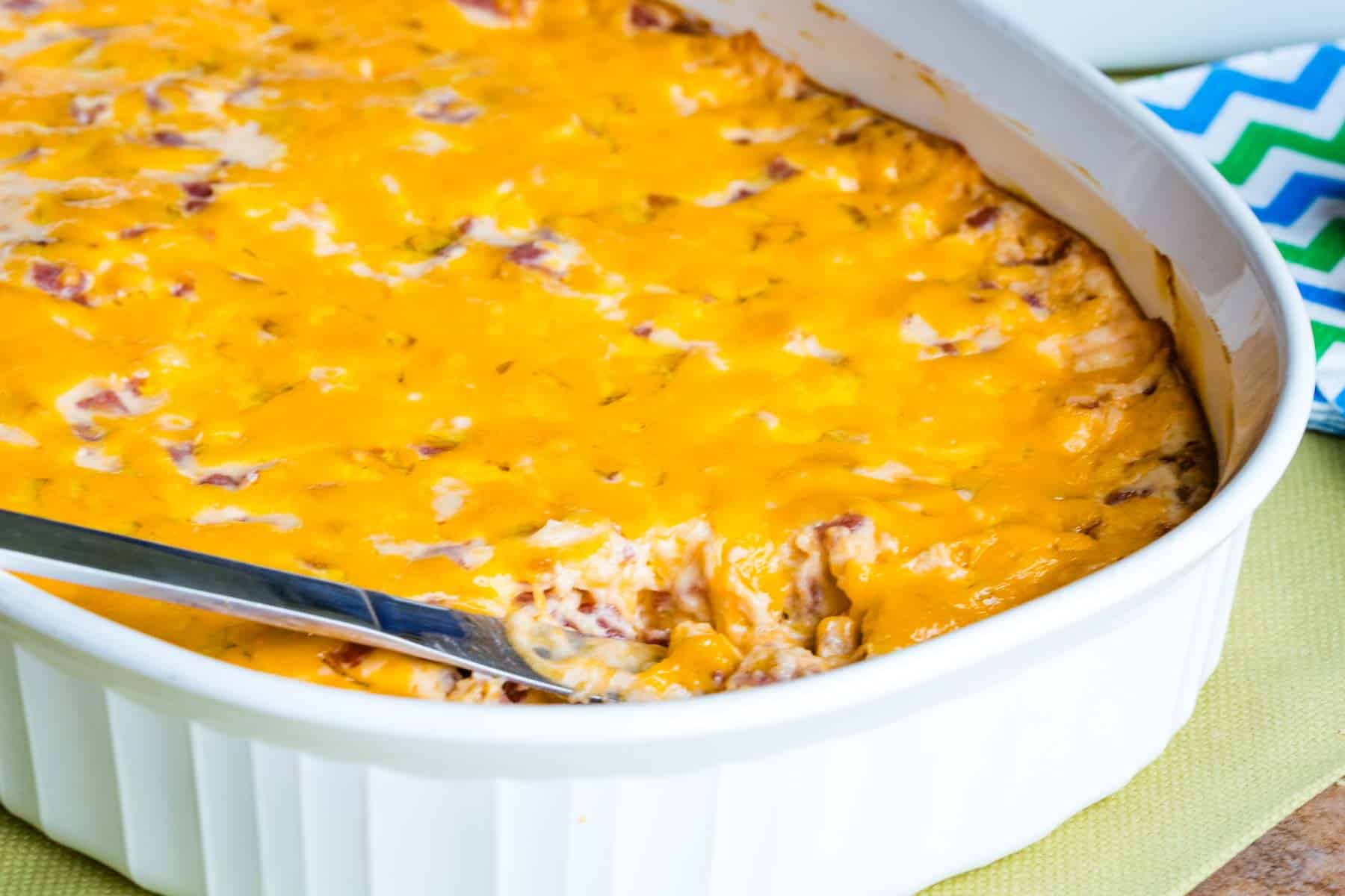 Cheesy Pork Roll Dip in a white casserole dish with a small knife in it.