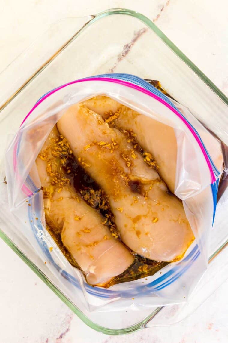 Overhead view of chicken breasts combined with Asian chicken marinade inside a zip-top bag.