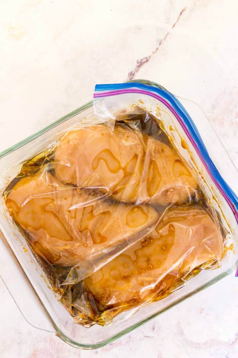 Chicken breasts marinating in a sealed bag placed inside a glass baking dish.