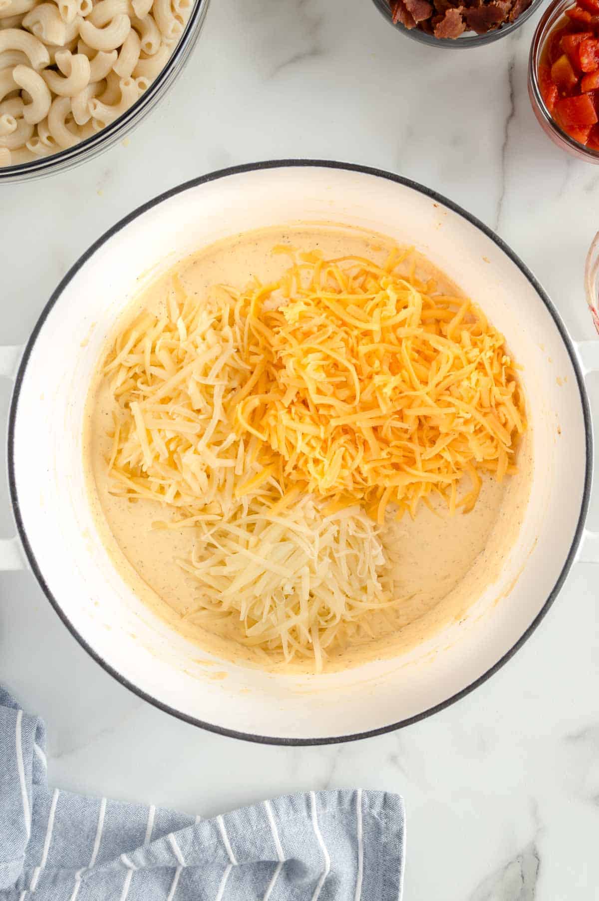 Three kinds of shredded cheese added to the cream sauce in the pot.