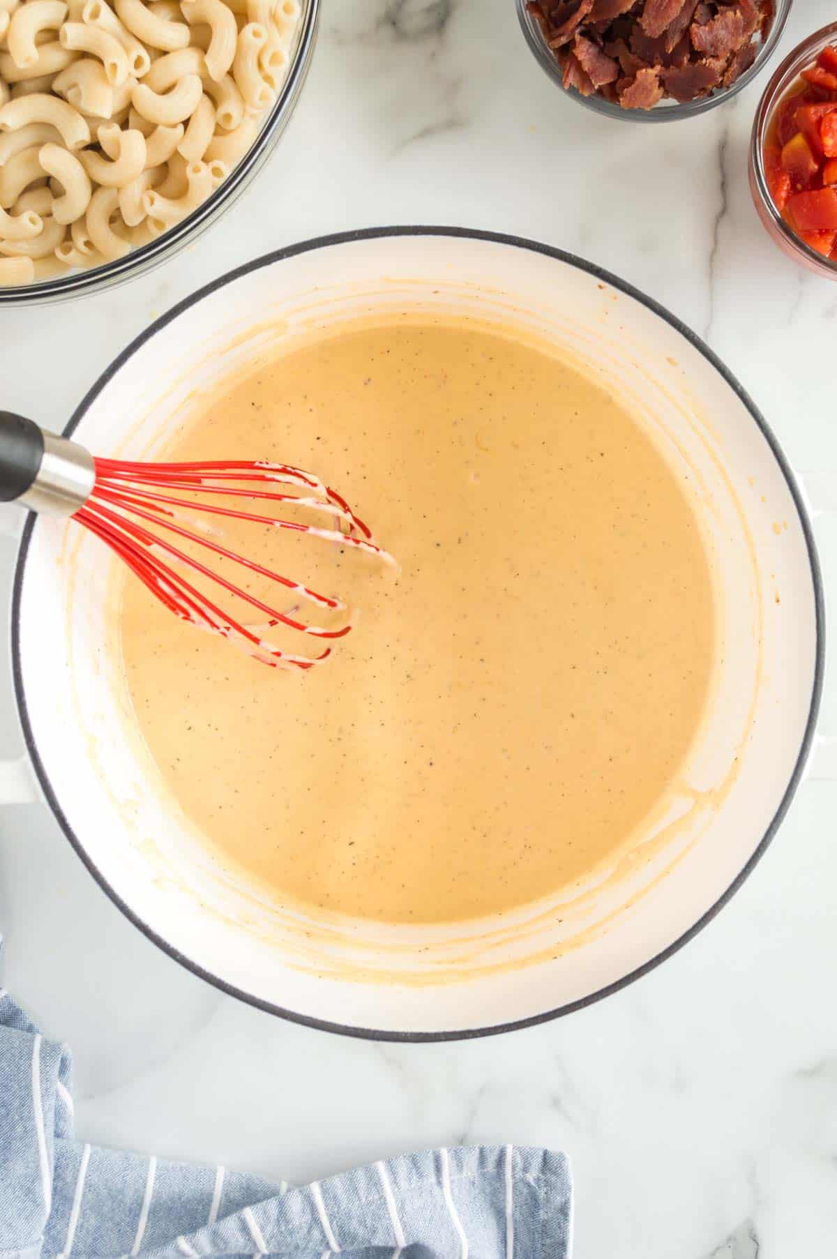 A pot of cheese sauce with a whisk.