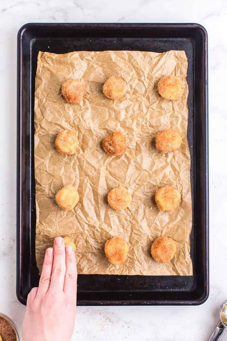 Using fingers to press down balls of cookie dough covered in cinnamon sugar.