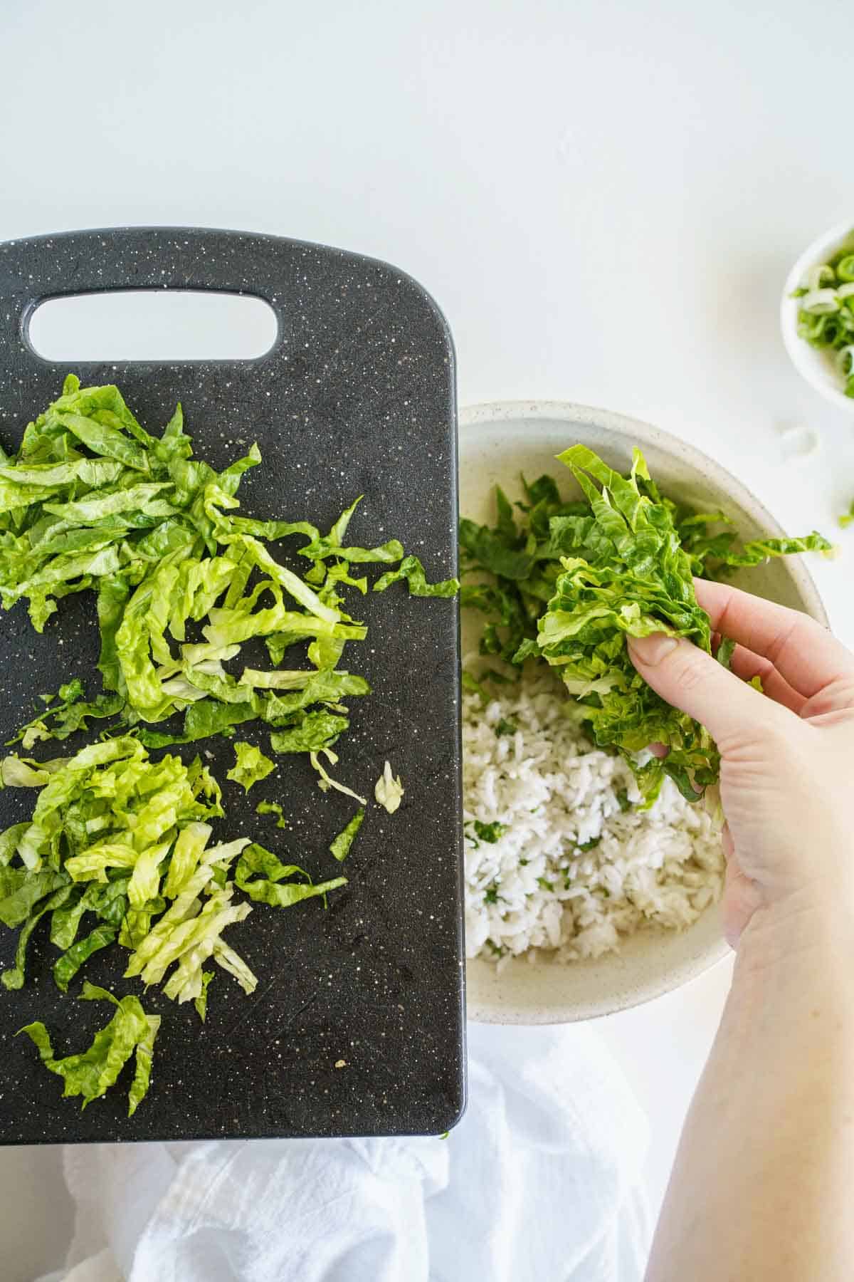 A Hand Adding Chopped Lettuce to a Bowl of Cilantro Rice.