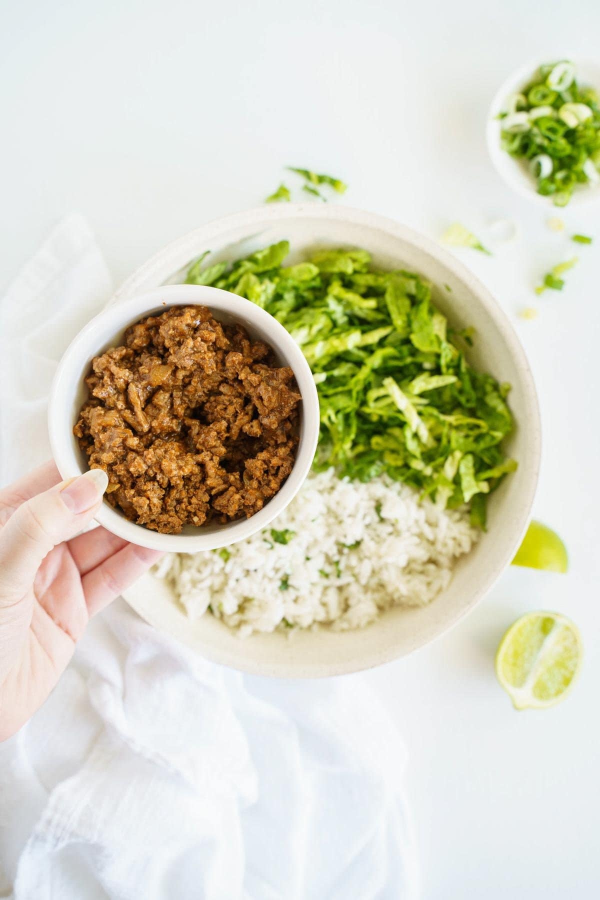 A bowl of taco meat being hels over the greens and grains bowl base.