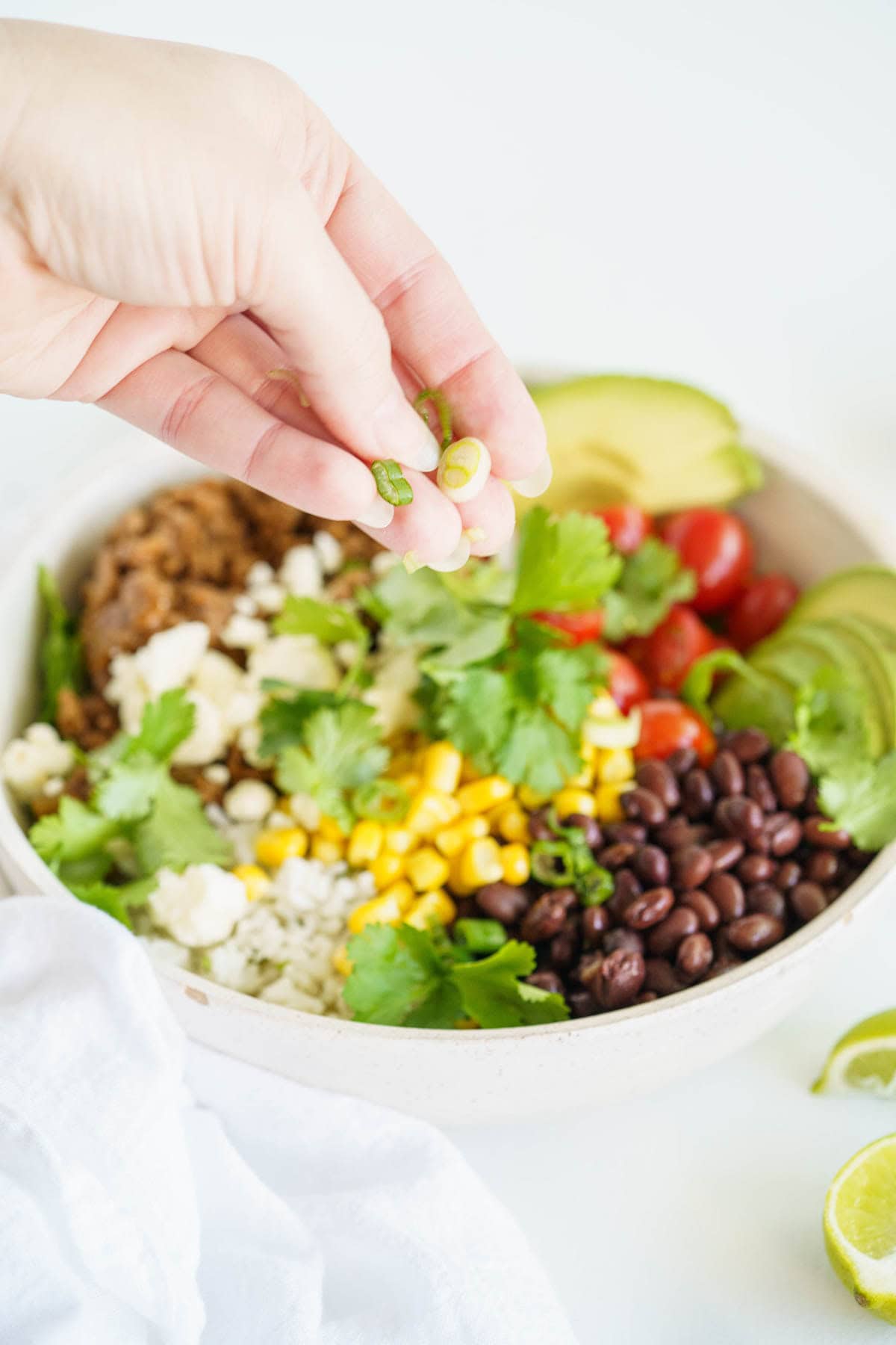 A hand sprinkling scallions over a burrito bowl.