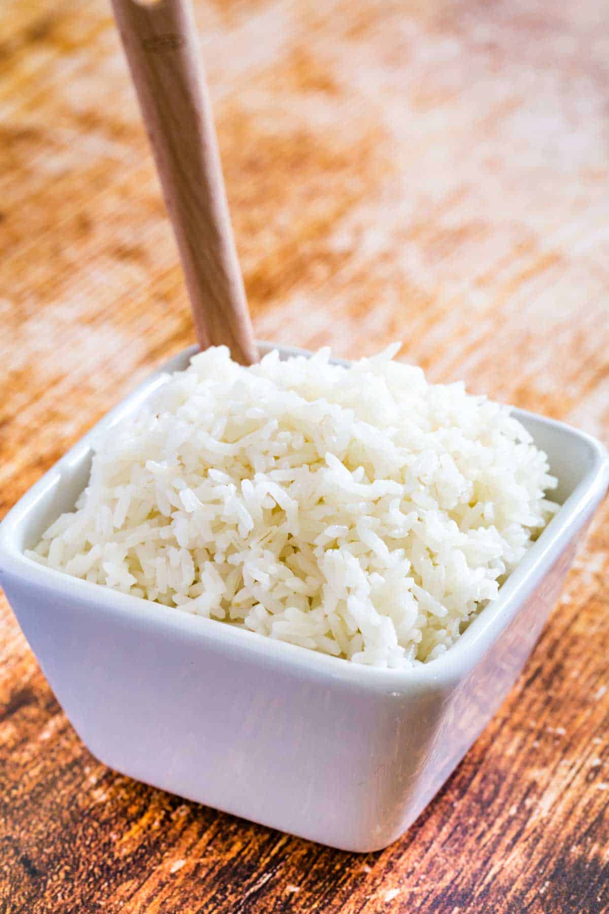 Jasmine rice in a square bowl with a wooden spoon.