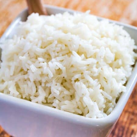 Jasmine rice in a square bowl with a wooden spoon.