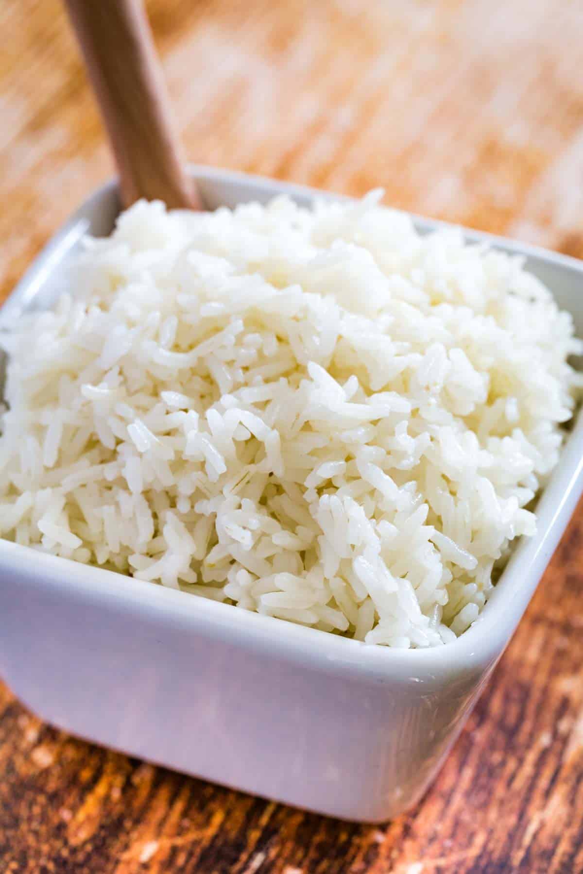 Jasmine rice in a square bowl with a wooden spoon.