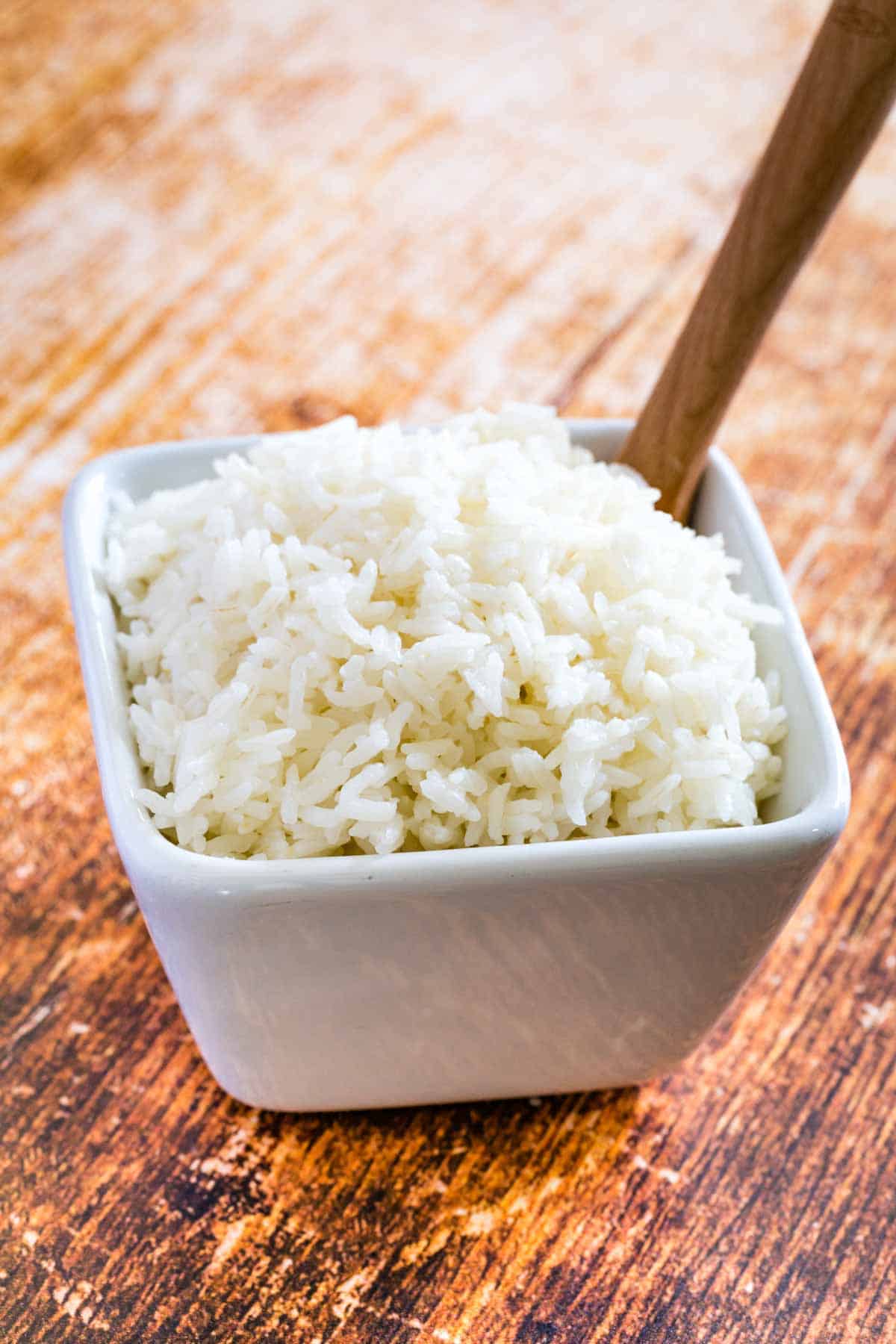 Jasmine rice in a square bowl with a wooden spoon.