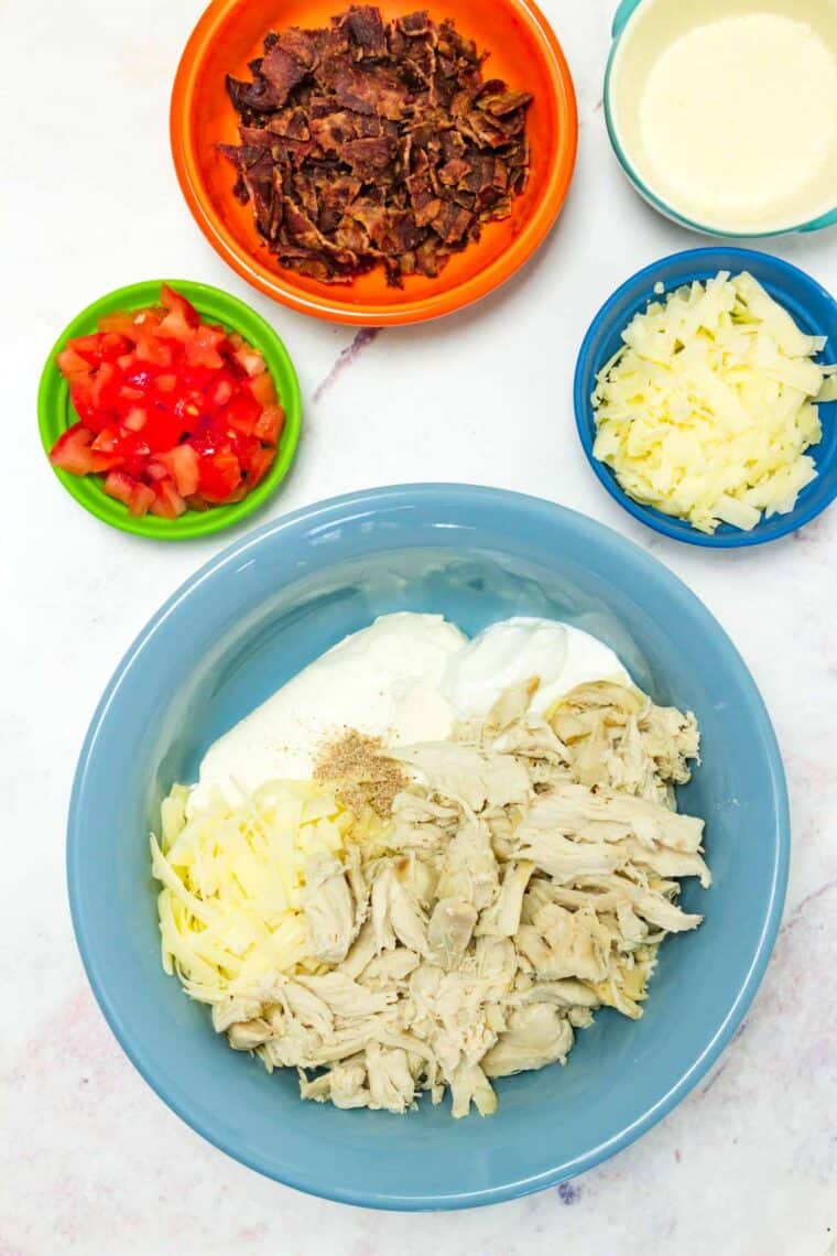 Turkey, cheese, and yogurt in a blue bowl with bowls of other ingredients around it.