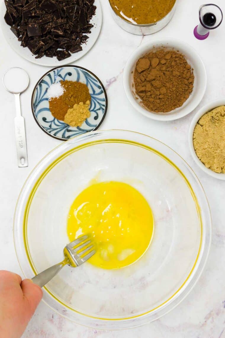 Eggs in a bowl being beaten with a fork with the other cookie ingredients around it on the counter.