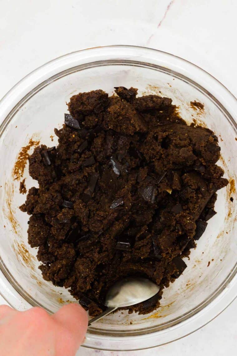 Cookie dough being scooped out of a glass bowl with a tablespoon measuring spoon.