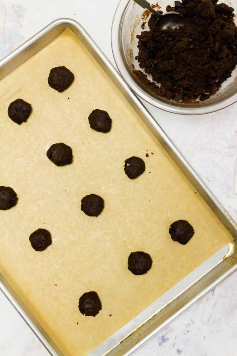 Chocolate cookie dough balls on a parchment-lined baking sheet.