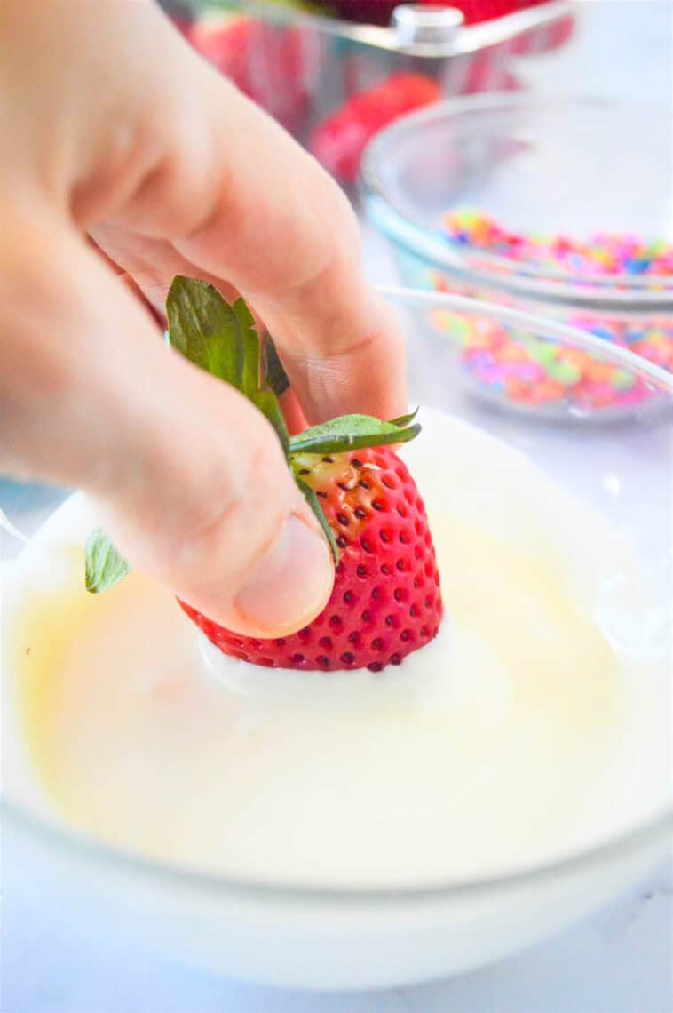 Dipping a strawberry into melted white chocolate.