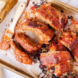 Cut up barbecue baby back ribs on a baking sheet with a brush covered with sauce.